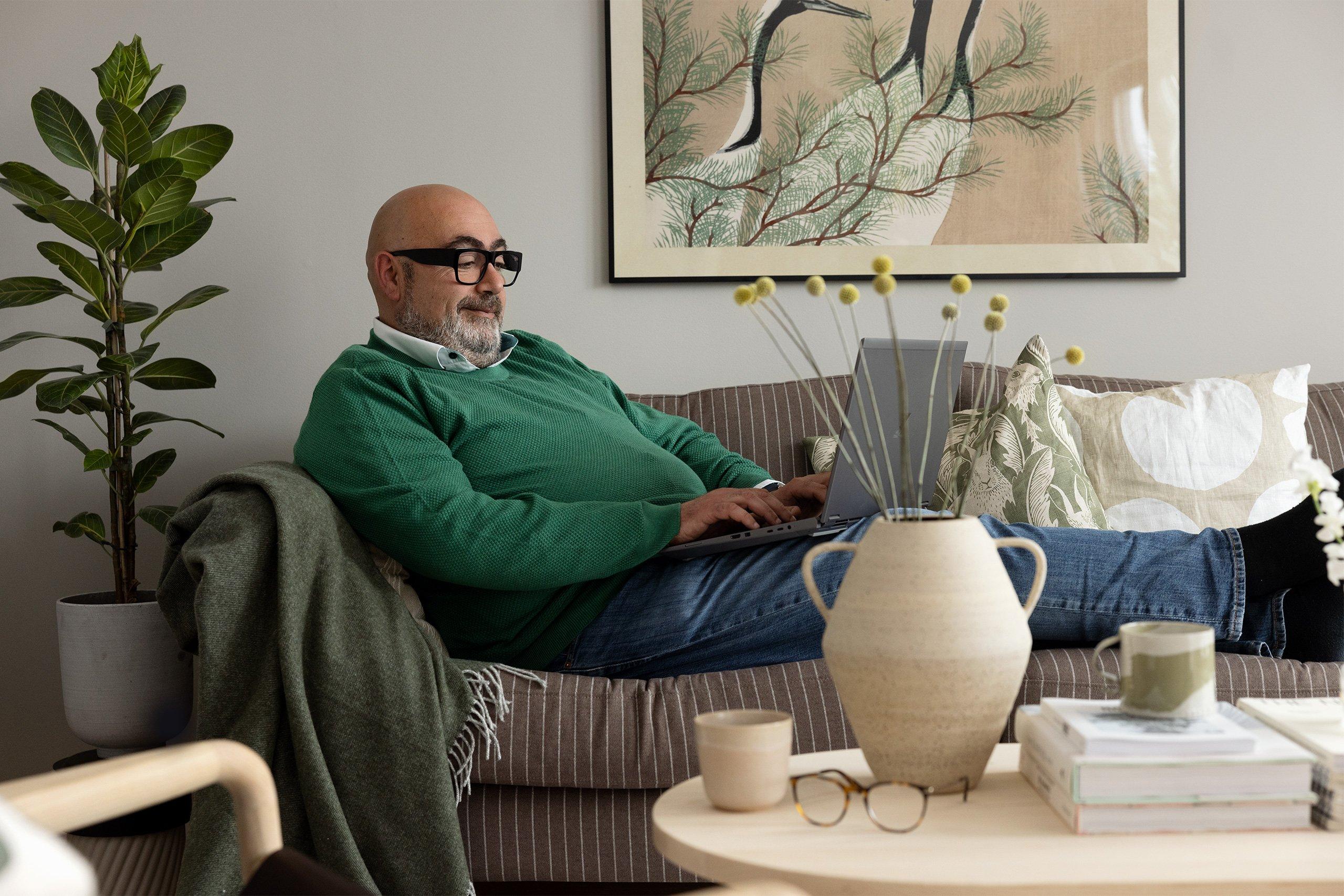 Äldre man sitter bekvämt i en soffa med en laptop i sitt knä.