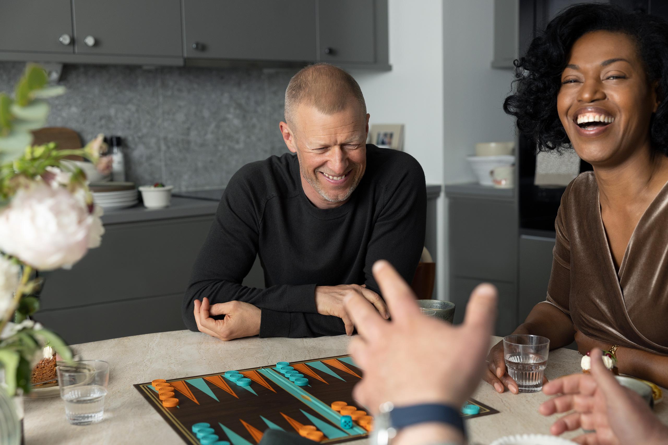 Några vuxna spelar spel och skrattar vid ett köksbord.